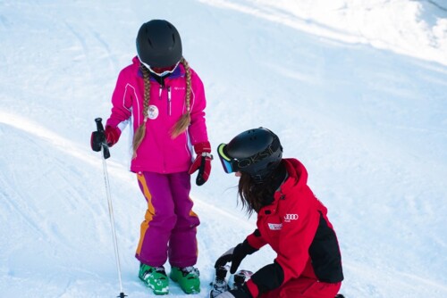 Ski instructor kneeling in the snow to adjust a ski for a child