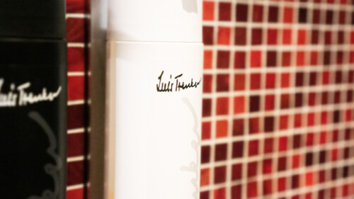 Dispenser with the Luis Trenker signature in front of a red mosaic wall