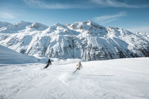 Two skiers on a wide groomed piste in the Obergurgl-Hochgurgl ski area